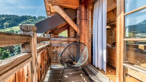 Un balcon en bois avec une chaise, une fenêtre et une vue sur un paysage montagneux.