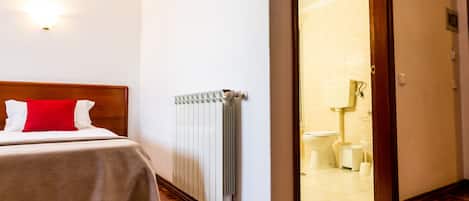 Una habitación de hotel con cama, un radiador y vistas al baño.