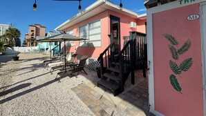 A building with a pink exterior, a staircase, outdoor seating with umbrellas, and a string of lights. - 3's Company-"Villa Janet"- 1 Block from Gulf of Mexico, 300 feet to the Gulf (Englewood)