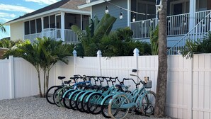 A row of teal bicycles parked against a white fence in front of a house with a porch and string lights. - 3's Company-"Villa Janet"- 1 Block from Gulf of Mexico, 300 feet to the Gulf (Englewood)