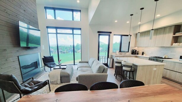 A spacious living room with a large wooden dining table, a sofa set, and a TV mounted on the wall. - Perfect Hot Tub, Seconds from Skiing, Heated pool! (Park City)