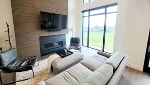 A modern living room with a fireplace, leather chairs, and a large window offering a view of the outdoors. - Perfect Hot Tub, Seconds from Skiing, Heated pool! (Park City)