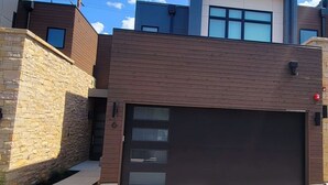 A modern two-story house with a garage, stone wall, and a large window on the upper floor. - Perfect Hot Tub, Seconds from Skiing, Heated pool! (Park City)