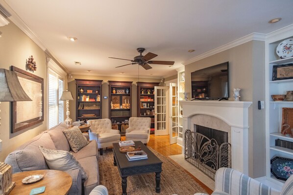 A spacious living room with a fireplace, a ceiling fan, and a large bookshelf.