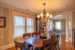 A dining room with a wooden table, chairs, a chandelier, and a vase with flowers.
