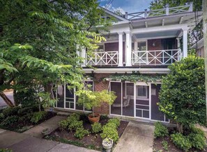 A two-story house with a balcony, brick exterior, and a garden with various plants.