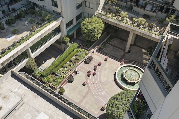 Eine Luftaufnahme eines Innenhofs mit einem zentralen, kreisförmigen Garten, umliegenden Gebäuden und einer Treppe, die zu einer oberen Ebene führt.