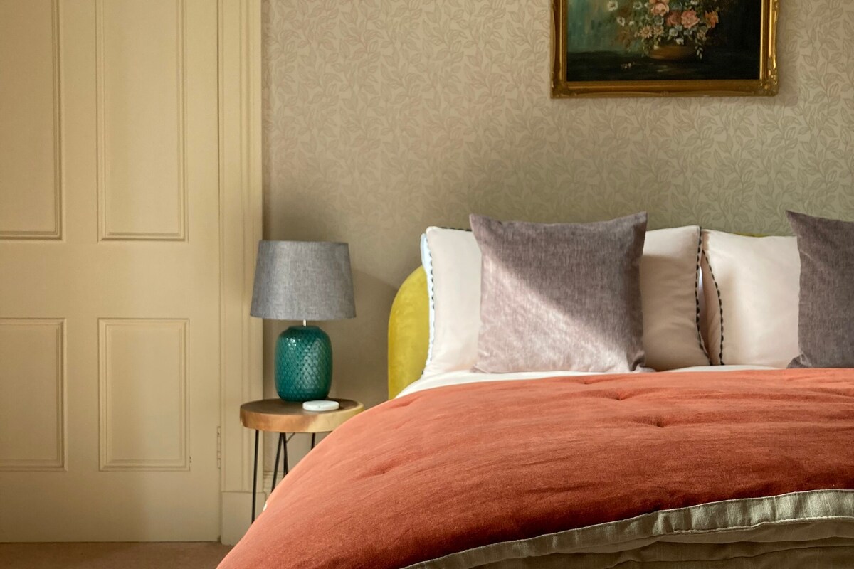 Un dormitorio con cama, almohadas, una lámpara y un cuadro en la pared.