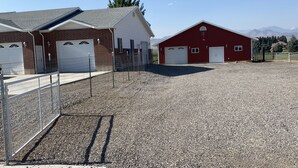 A gravel parking area with two buildings, one brick and one red, with white garage doors. - Country Farmhouse (Monroe)