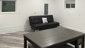 A room with a ceiling fan, a black sofa with a pillow, a wooden table with chairs, and a window. - Country Farmhouse (Monroe)