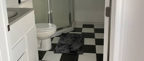 Pieni kylpyhuone, jossa on wc, suihkukaappi ja ruutukuviollinen lattia.