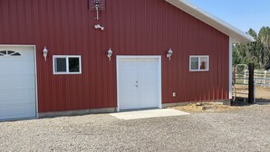 A red barn with a white garage door, two windows, and a ventilation system on the roof. - Country Farmhouse (Monroe)