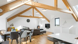 A spacious loft with exposed wooden beams, a dining area with modern furniture, a cozy fireplace, and a large window providing natural light. - Perfect for a Cornish getaway, Cedar House is located just outside the hustle and bustle of St Agnes (St Agnes)