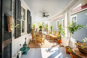 Une véranda abritée avec une table et des chaises, des plantes en pot et un ventilateur de plafond.