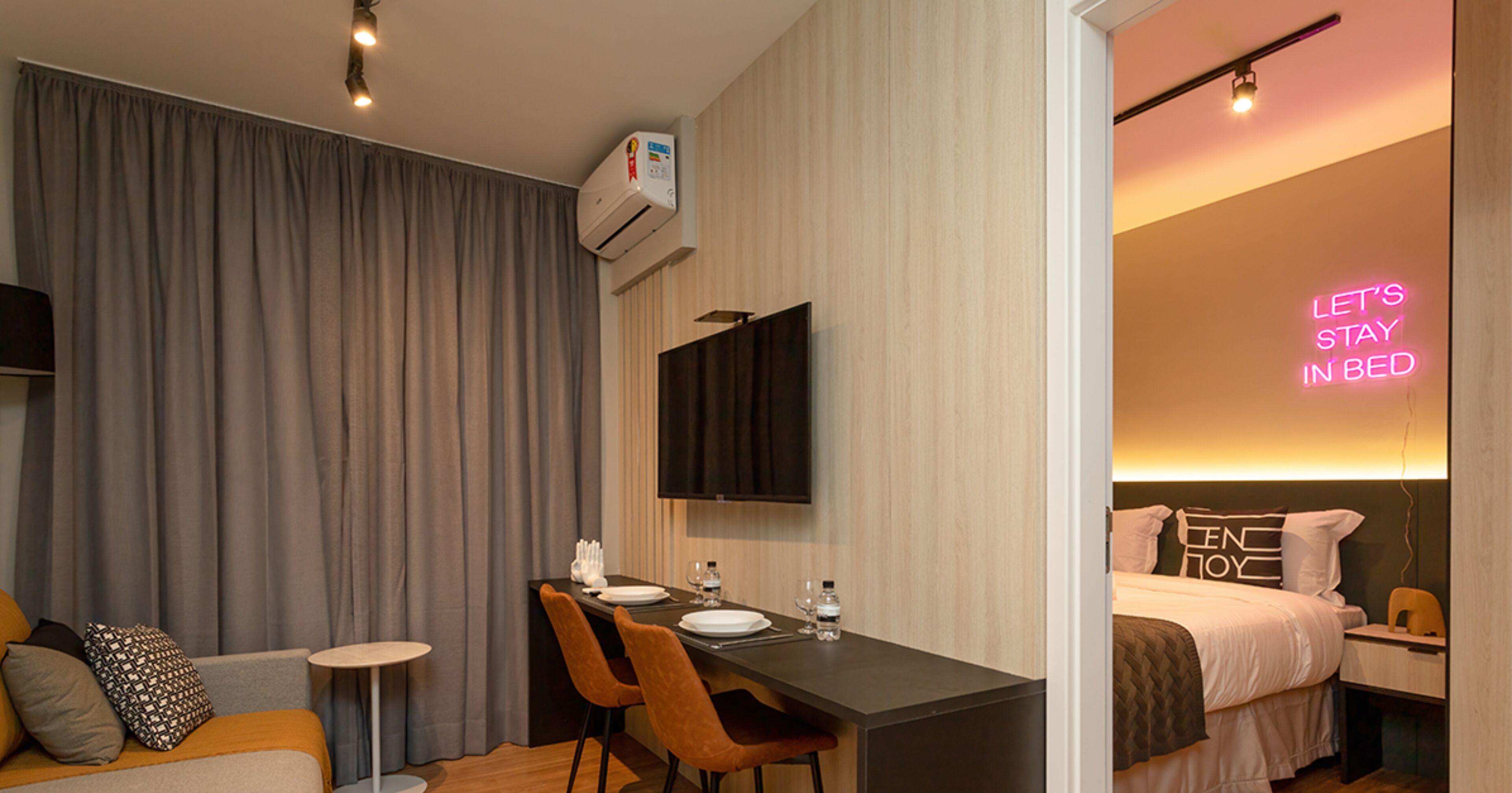 Ein modernes Hotelzimmer mit einem Bett, einem Schreibtisch mit Stühlen, einem Flachbildfernseher und einer Neonreklame.