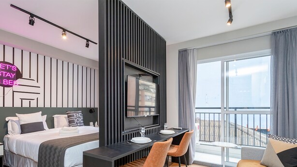 Habitación de hotel moderna con cama, escritorio y balcón con vistas.