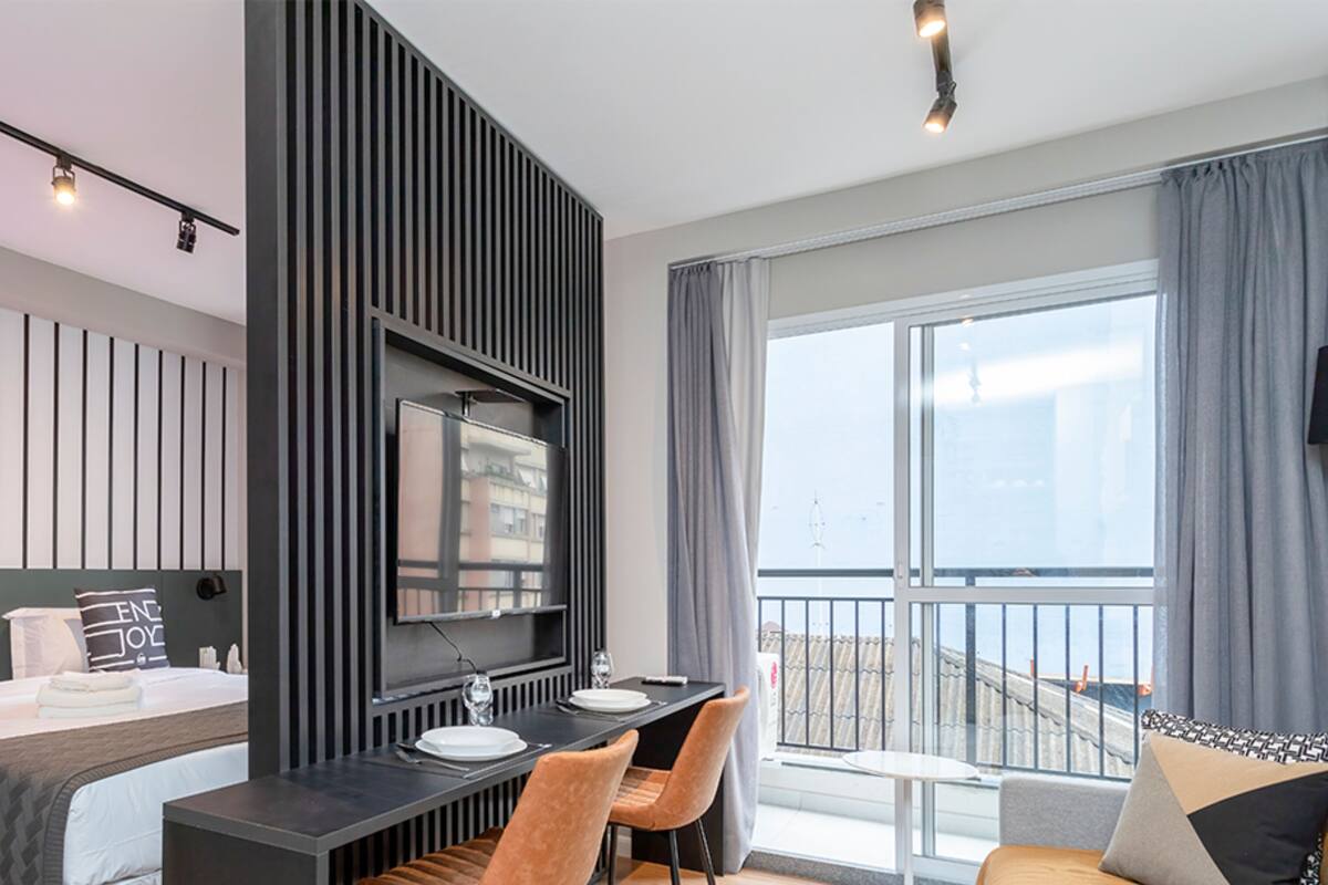 A modern hotel room with a bed, a desk, and a balcony with a view.