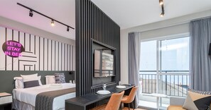 A modern hotel room with a bed, a desk, and a balcony with a view.