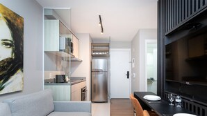 Una cocina moderna con un refrigerador de acero inoxidable, un comedor con una mesa y sillas negras, y un televisor de pantalla plana grande montado en la pared.