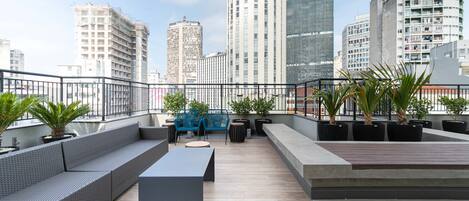 A rooftop terrace with seating, potted plants, and a city skyline view.
