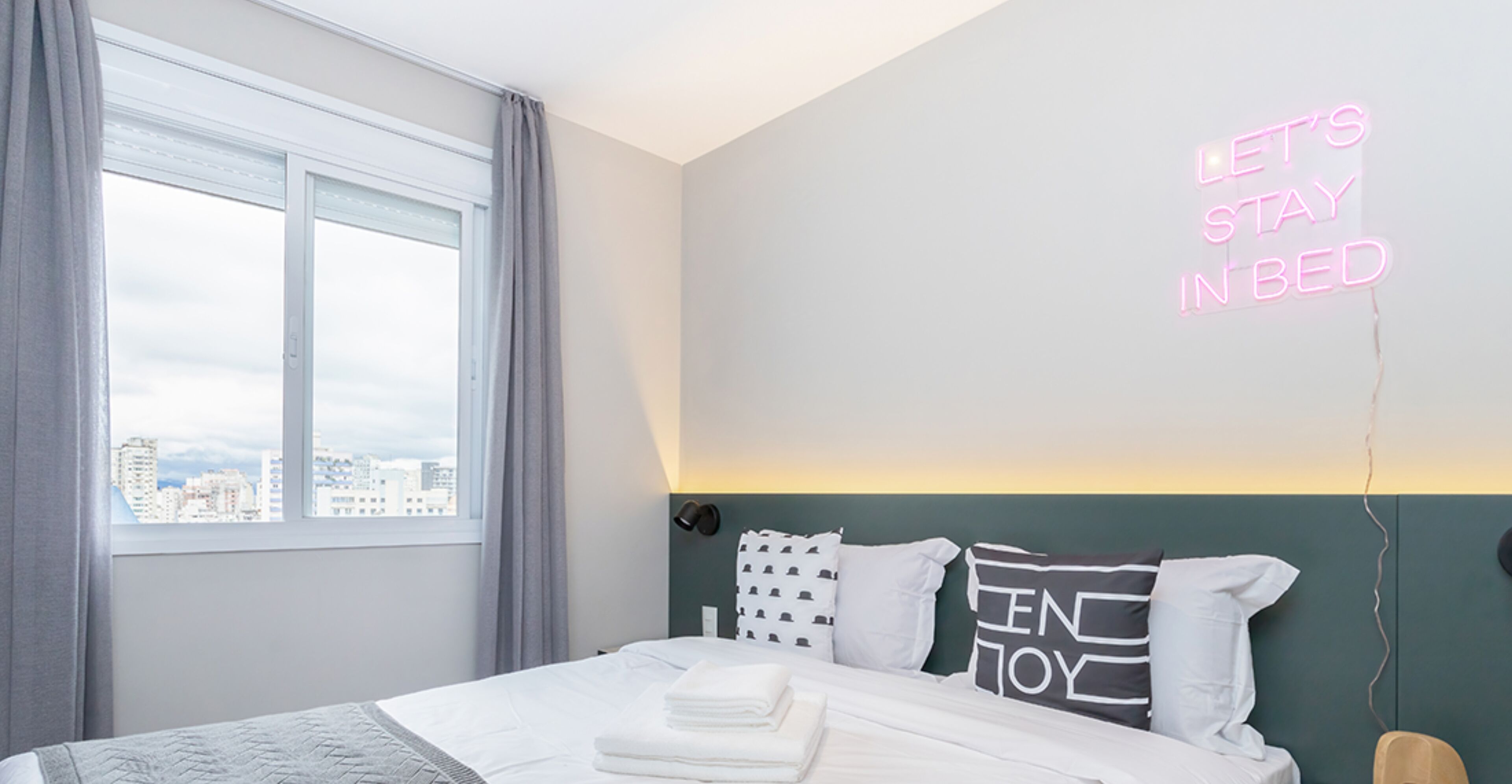 Une chambre d’hôtel moderne avec un lit, une vue sur la ville et un panneau lumineux au néon sur le mur.