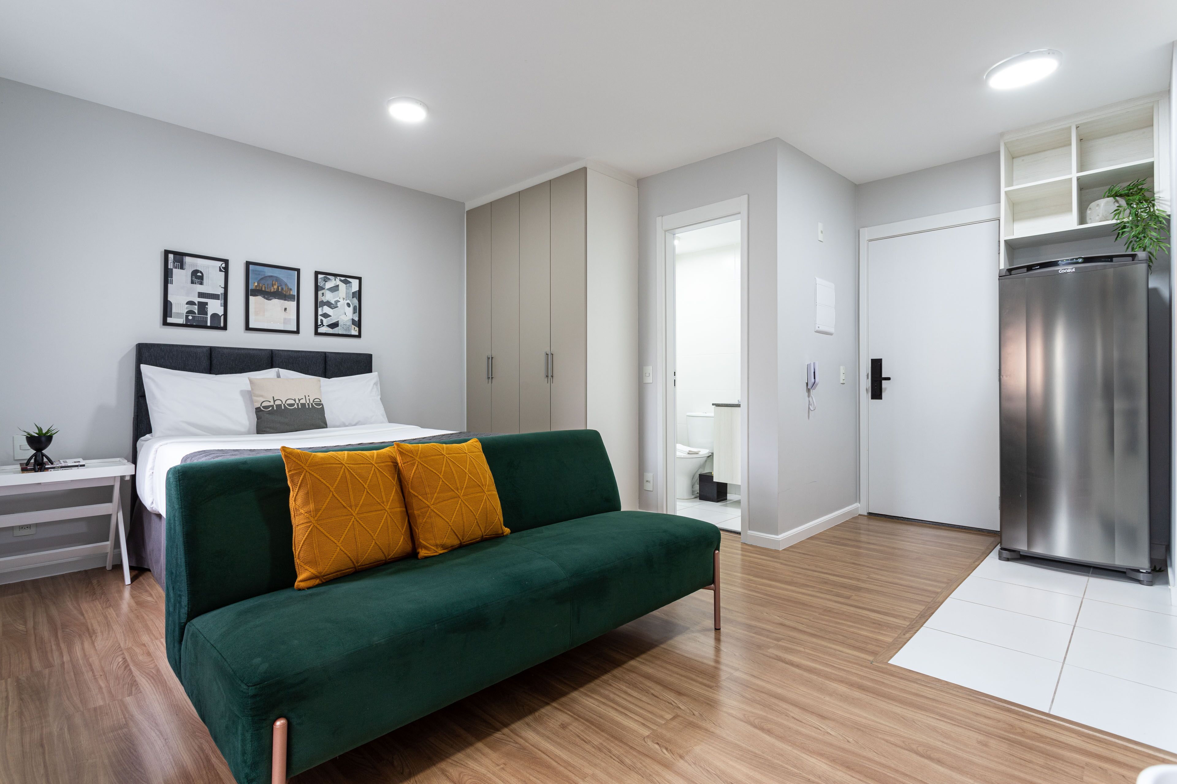 A modern bedroom with a green sofa, a bed with white bedding, and a white wardrobe.