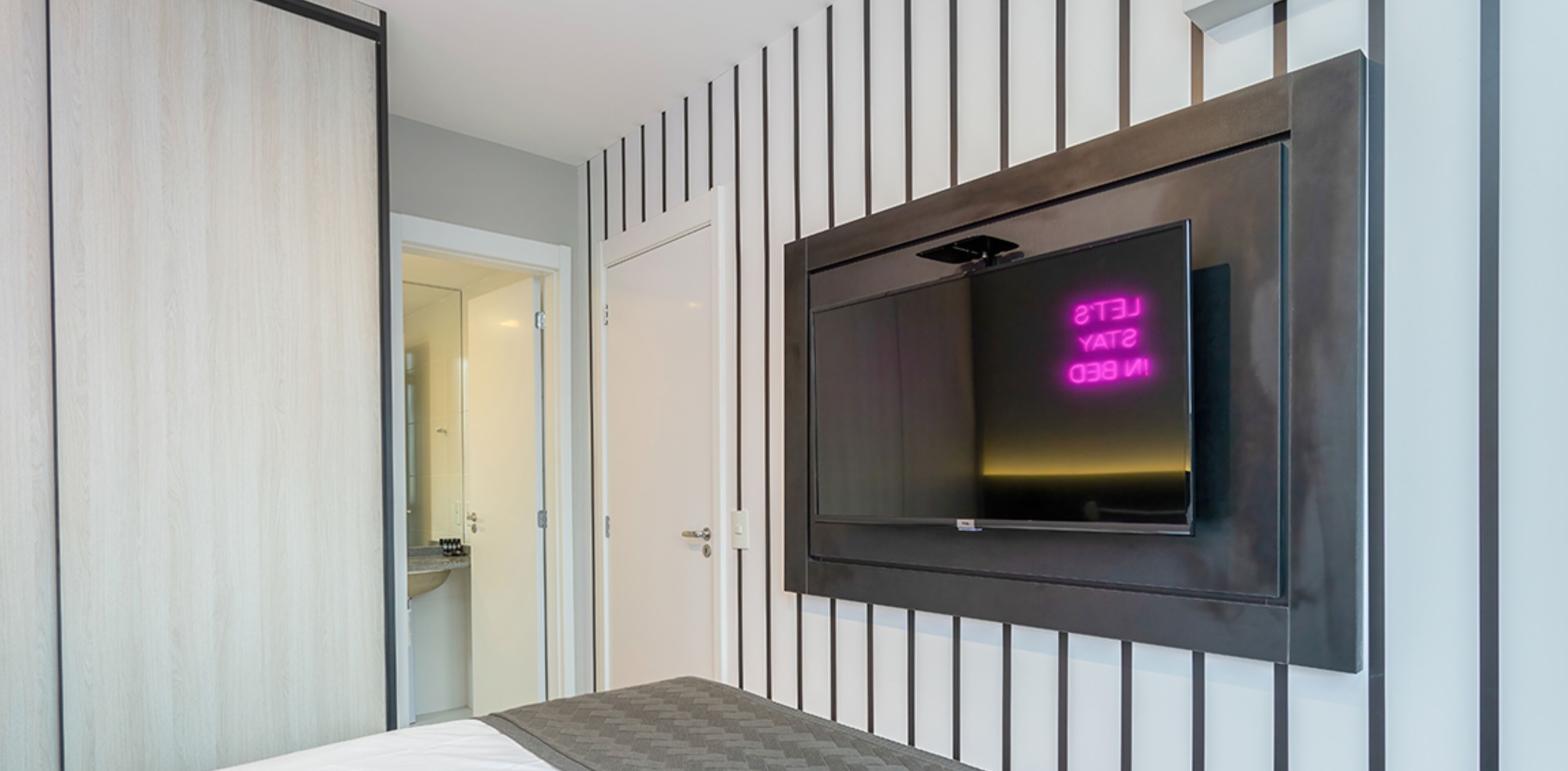 Une chambre d’hôtel moderne, équipée d’un lit, d’un téléviseur fixé au mur et d’une porte donnant accès à une salle de bain.
