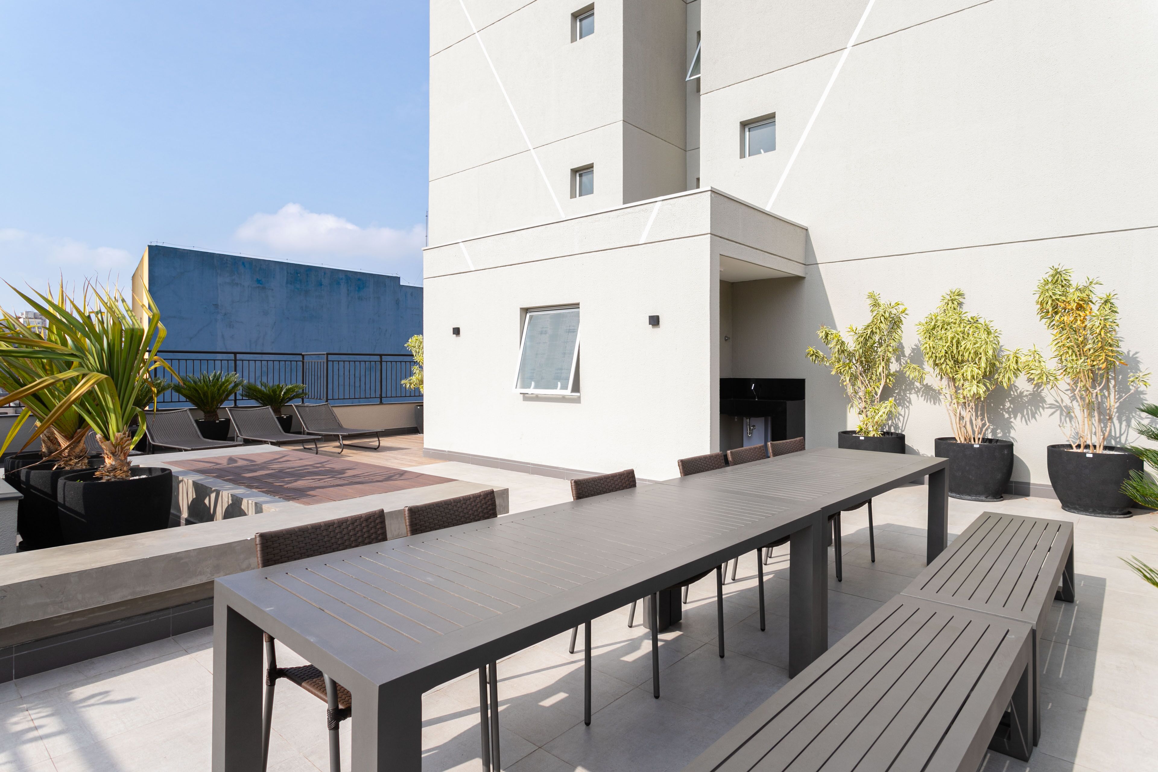Eine Dachterrasse mit einem langen Esstisch, Lounge-Stühlen und Topfpflanzen.