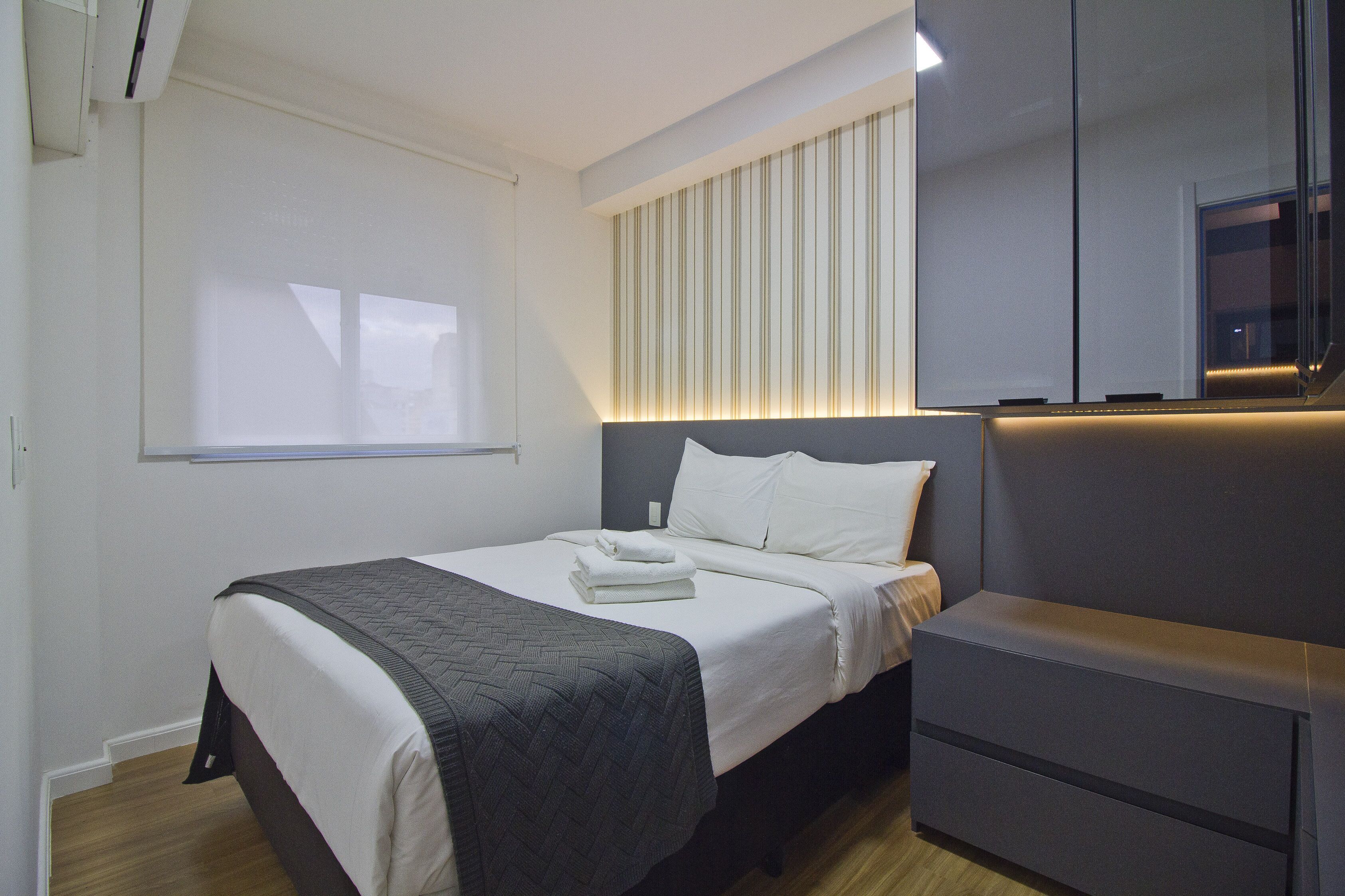 A modern hotel room with a neatly made bed, a bedside table, and a built-in TV.
