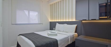 A modern hotel room with a neatly made bed, a bedside table, and a built-in TV.