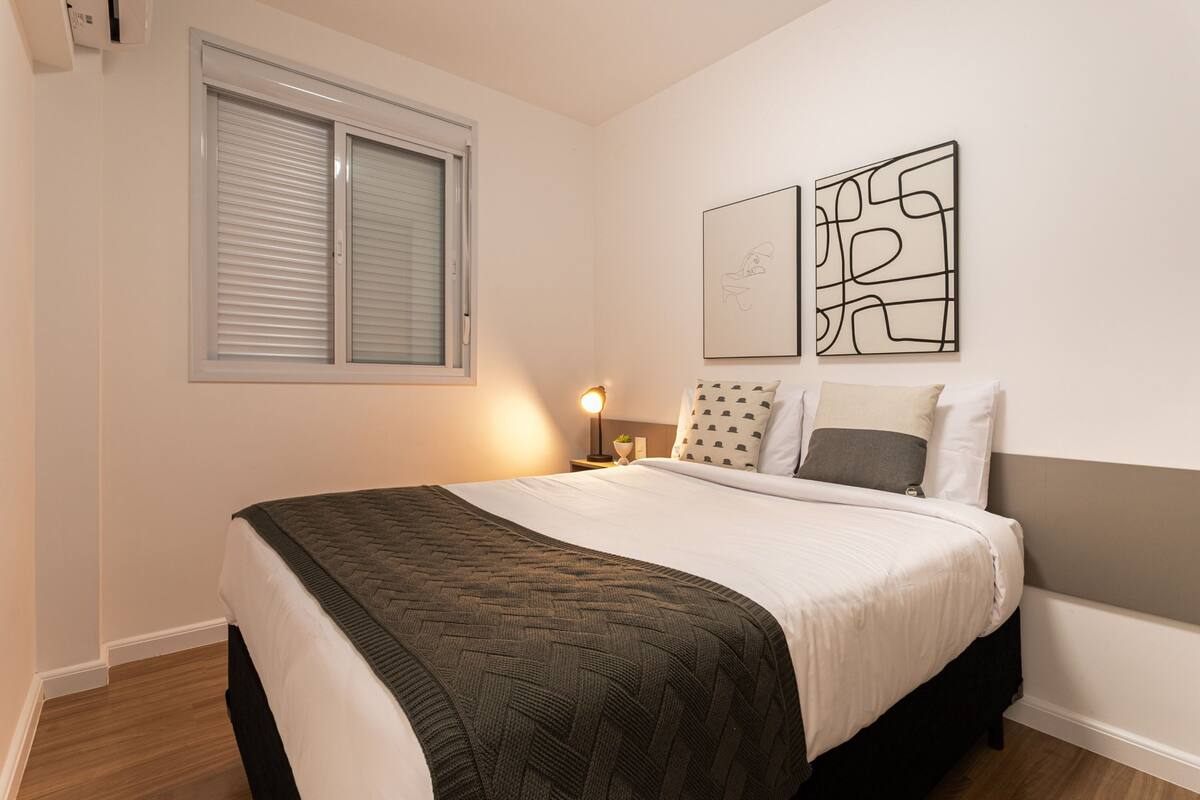 A neatly made bed with a patterned bedspread, a bedside lamp, and two abstract wall art pieces.