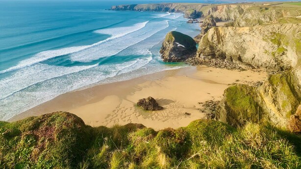 Un paysage côtier avec une plage de sable, des falaises rocheuses et une mer bleue et limpide.