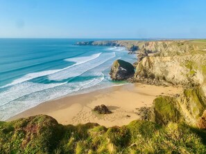 A coastal landscape with a sandy beach, rocky cliffs, and a clear blue sea.