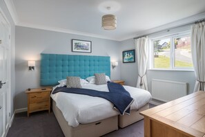 Quarto com cama grande, mesas de cabeceira, escrivaninha de madeira e janela com cortinas.