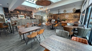 Un restaurant moderne doté de hauts plafonds, d’un bar et d’un espace aménagé avec des tables et des chaises.