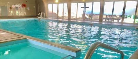Piscina interior con agua cristalina, un trampolín y vistas al exterior a través de amplios ventanales.
