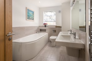 Uma casa de banho moderna com banheira, sanita e duas pias.