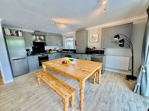 A modern kitchen with grey cabinets, a wooden dining table, and a bench.