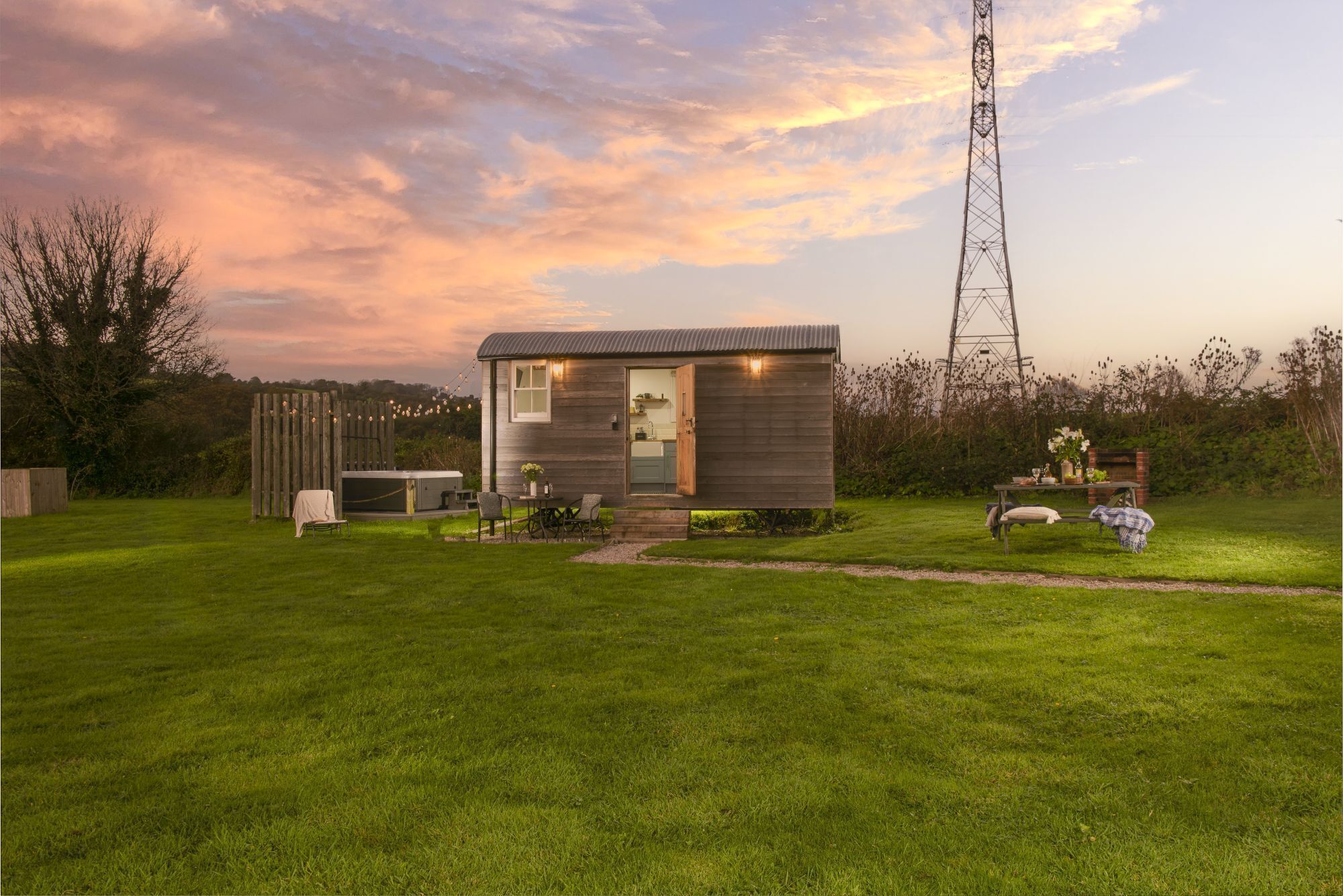A small, single-story cabin with a metal roof, a wooden deck, and a patio area with outdoor seating.
