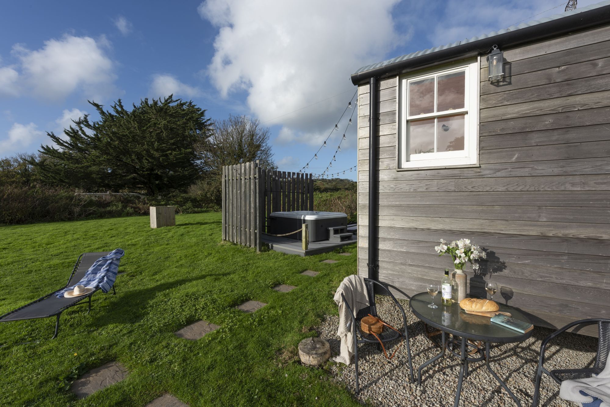A wooden house with a patio area, a hot tub, and a table with a loaf of bread and wine glasses.