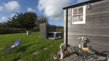 A wooden house with a patio area, a hot tub, and a table with a loaf of bread and wine glasses.