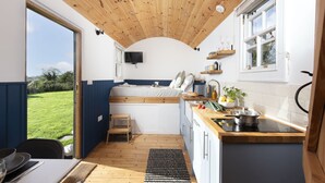 Une cuisine moderne et compacte, avec un plafond en bois, un petit coin repas et une vue sur un paysage verdoyant par une porte ouverte.