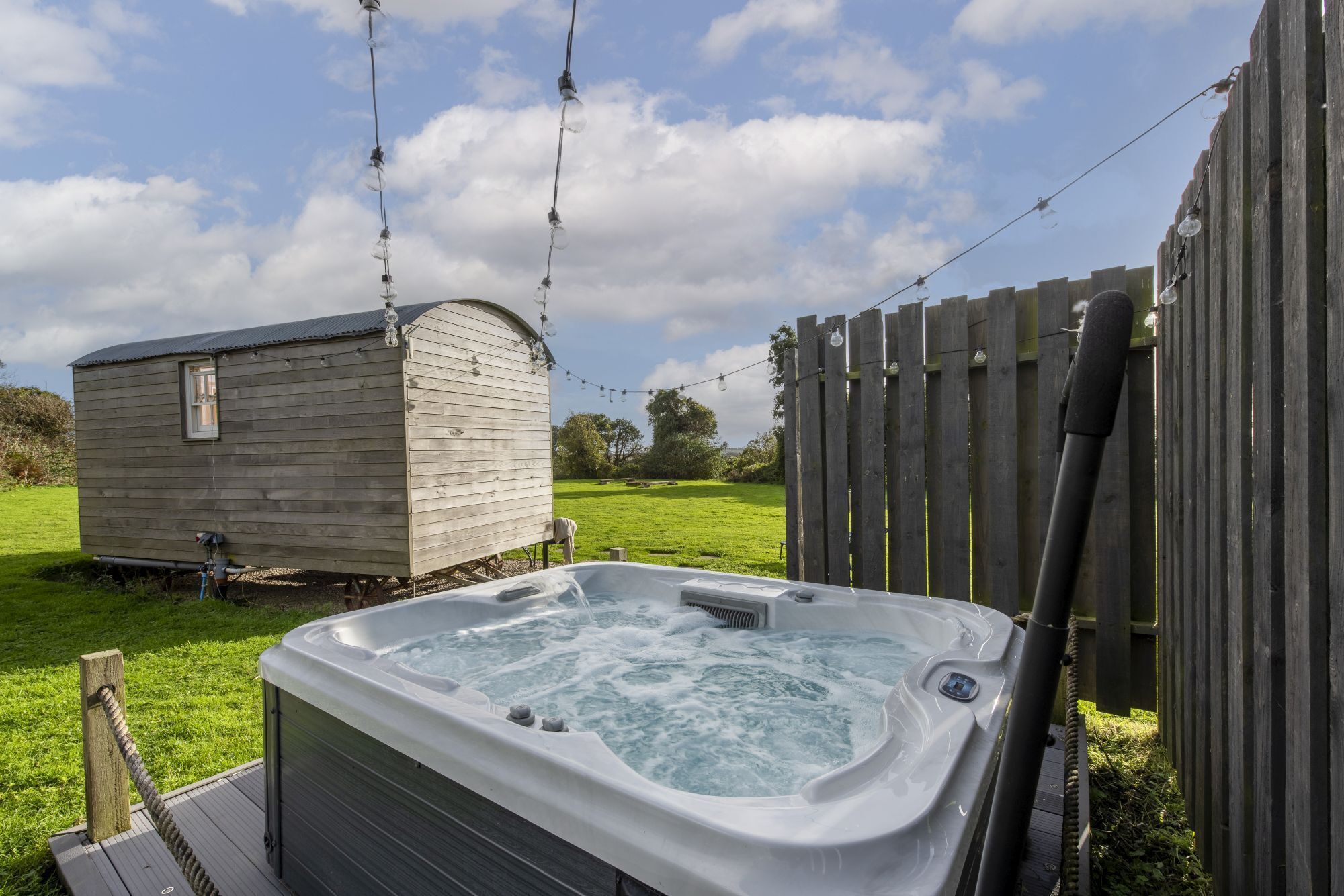 A hot tub in a backyard with a wooden deck, a small shed, and a wooden fence.