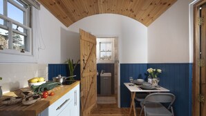 Une cuisine compacte avec un plafond en bois, un coin repas avec une table et des chaises, et une vue sur la salle de bain à travers une porte ouverte.