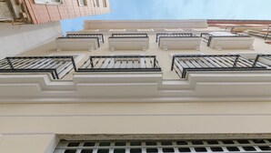 Fachada de edificio con varias unidades de aire acondicionado, una serie de balcones con barandillas negras y una rejilla de ventilación en la parte inferior.
