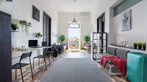A modern living room with a sofa, a dining area with chairs and a table, and a view of the city through an open door. - Bee Hostel (Limassol)