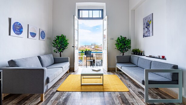 A modern living room with two grey sofas, a coffee table, and a yellow rug. There are two potted plants and a painting on the walls. - Bee Hostel (Limassol)
