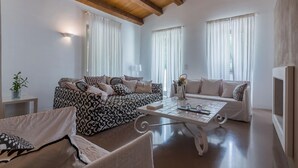 Ein geräumiges Wohnzimmer mit hohen Decken, zwei Sofas mit gemusterten Kissen, einem Couchtisch und einem Beistelltisch mit einer Pflanze.