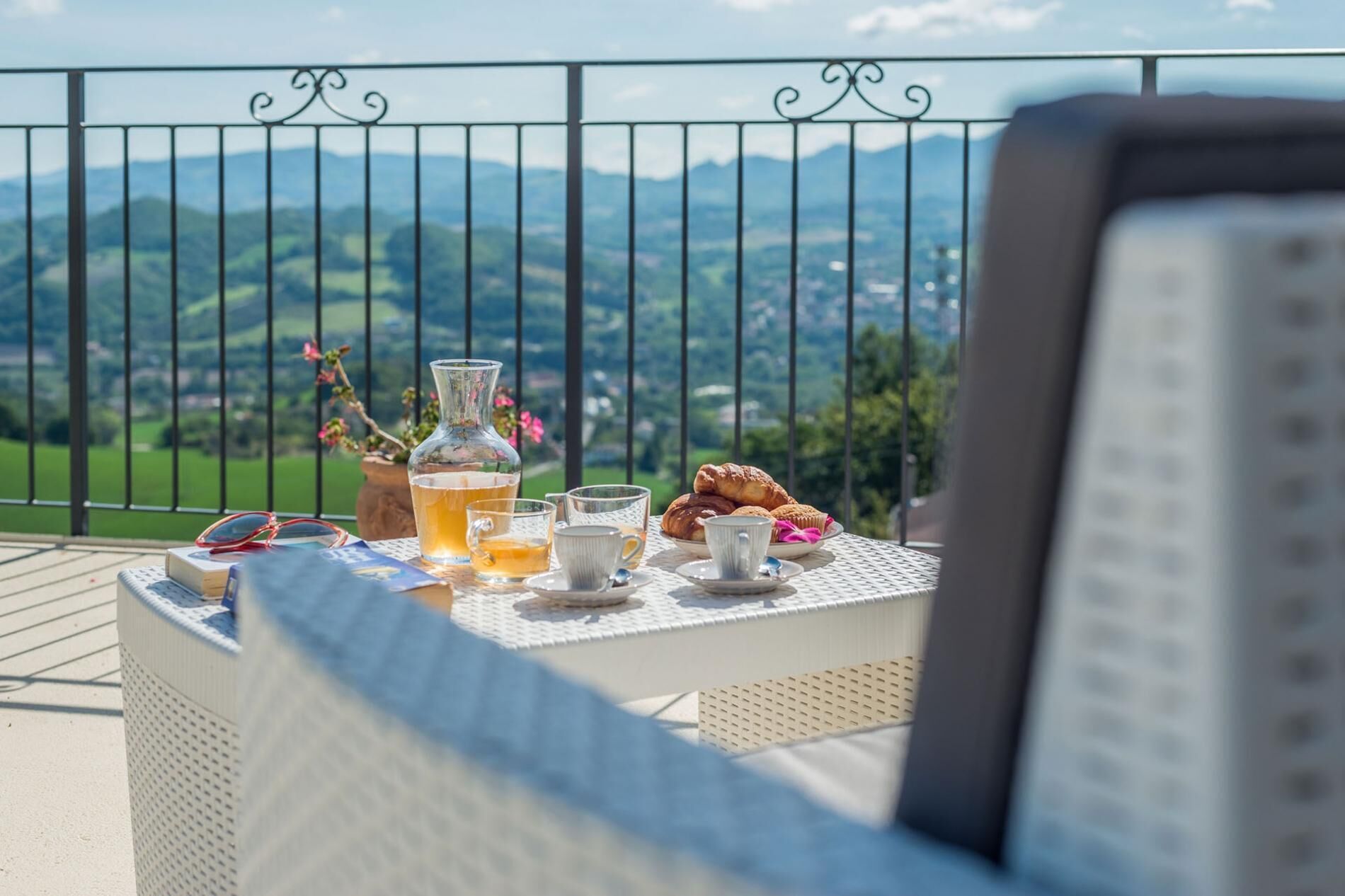 Une table avec des boissons, des pâtisseries et un vase de fleurs sur un balcon offrant une vue sur la montagne.