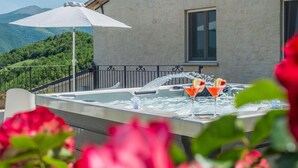 Ein Whirlpool mit zwei Martini-Gläsern, einem weißen Sonnenschirm und Blick auf grüne Hügel.